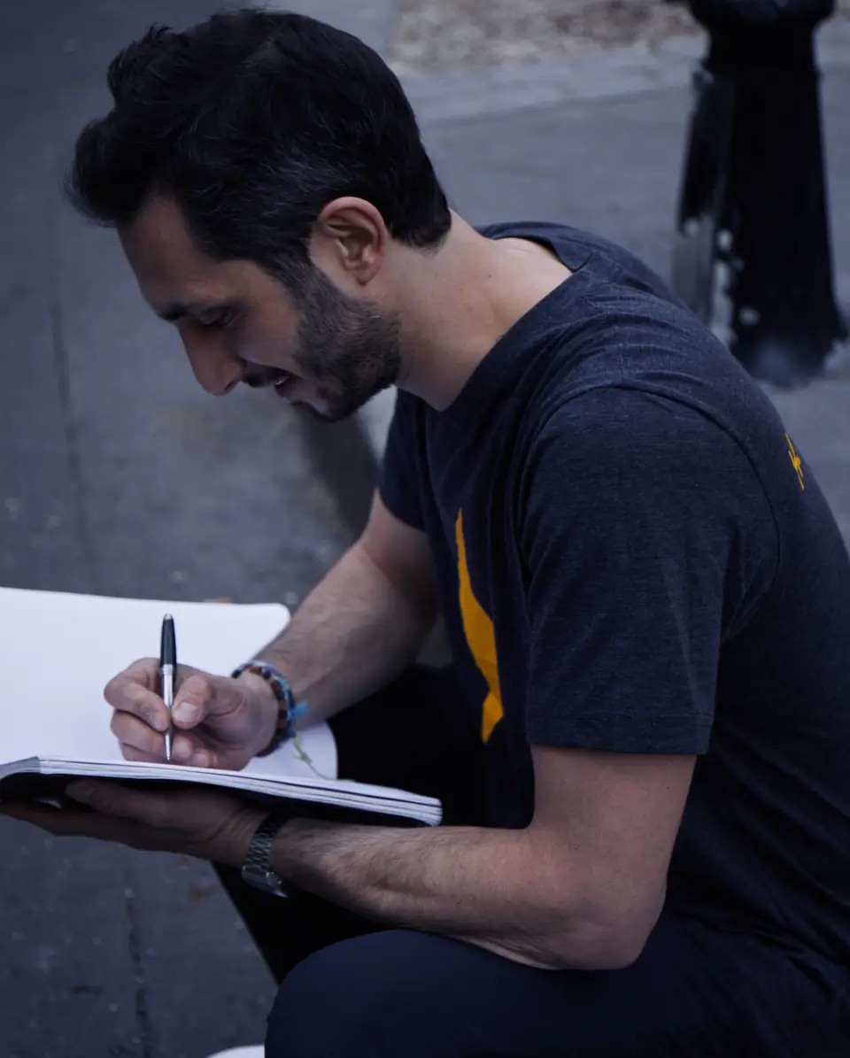 Un coach assis sur un trottoir écrit dans un carnet, tee-shirt à l'éclair jaune