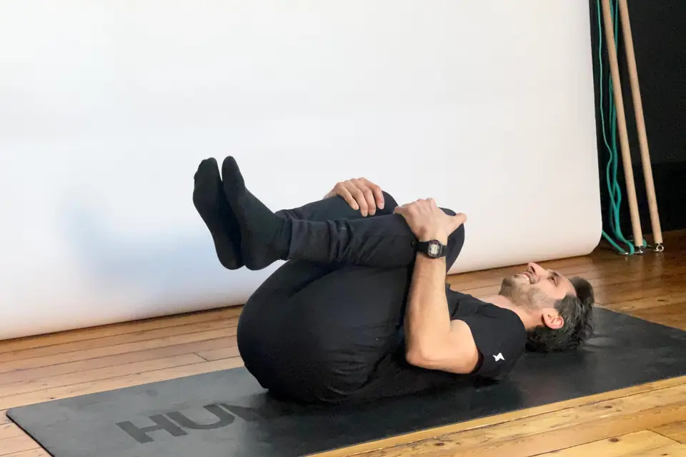 Un coach allongé sur le dos sur un tapis noir, les genoux serrés contre la poitrine pour relâcher le bas du dos