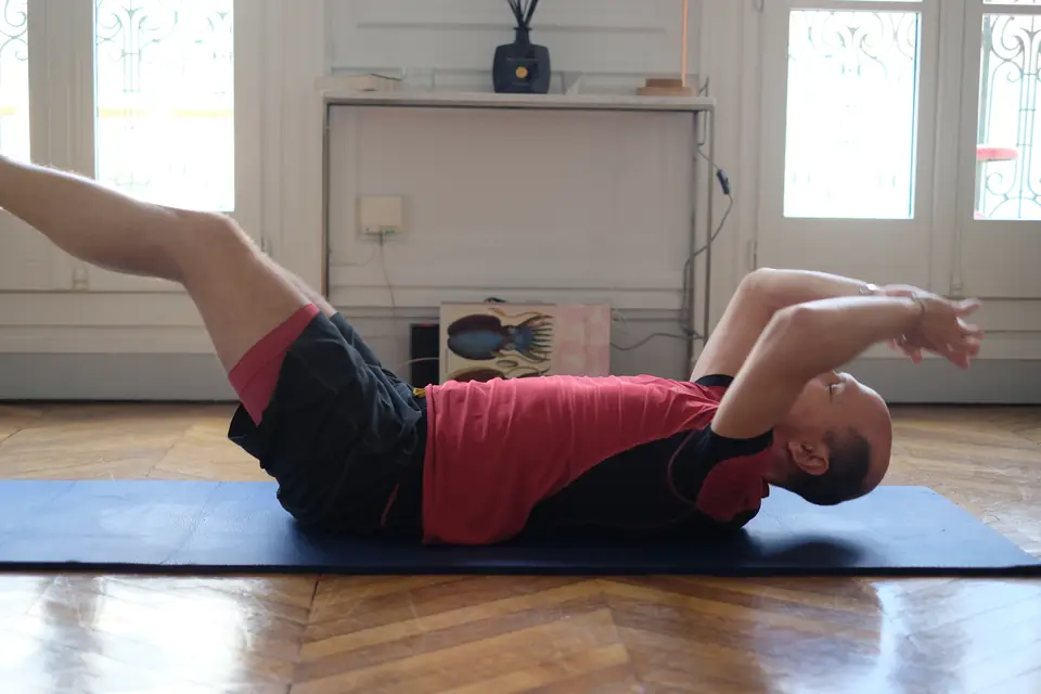 Homme allongé sur un tapis, bras et jambes tendus en gainage, dans un appartement parisien