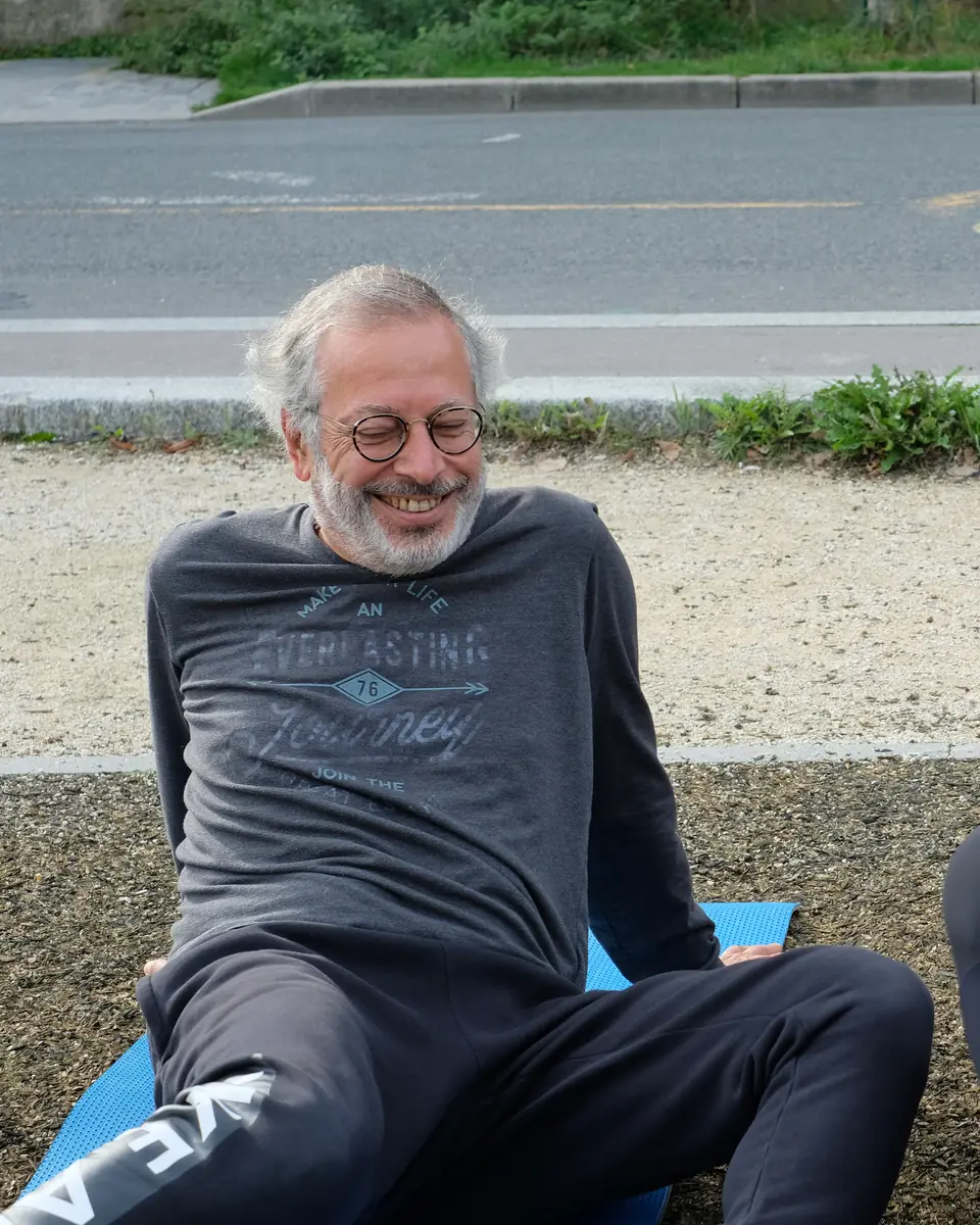 Homme aux cheveux gris et à lunettes, souriant, assis sur un tapis bleu au bord de la Seine