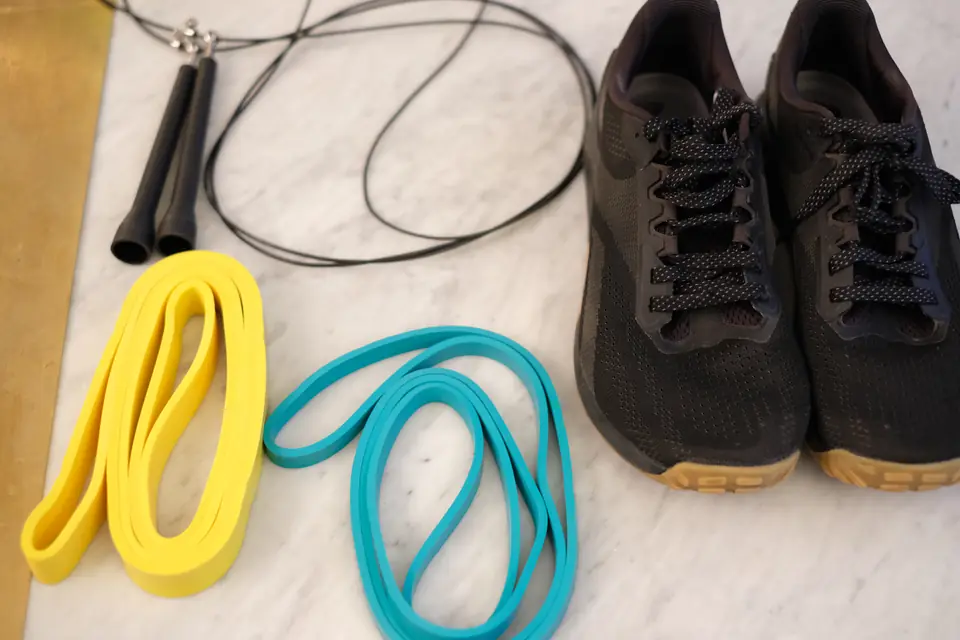 Corde à sauter, deux élastiques de résistance, un jaune et un turquoise, et une paire de chaussures de sport posés sur un plan en marbre
