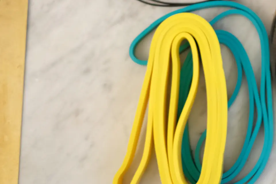 Deux élastiques de résistance, un jaune et un turquoise, roulés à plat à côté d'une corde à sauter