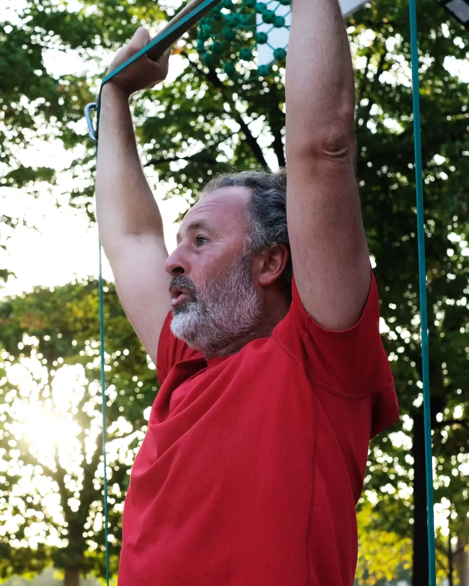 Senior barbu tirant un élastique bras tendus au-dessus de la tête, sous les arbres