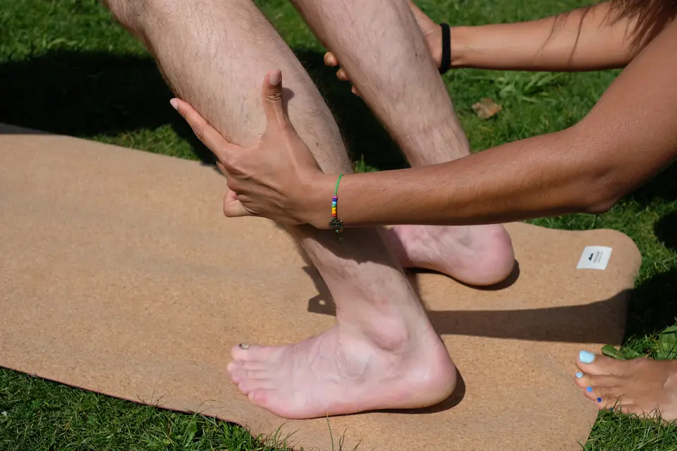 Une main tient le mollet d'une personne debout pieds nus sur un tapis de liège, sur l'herbe